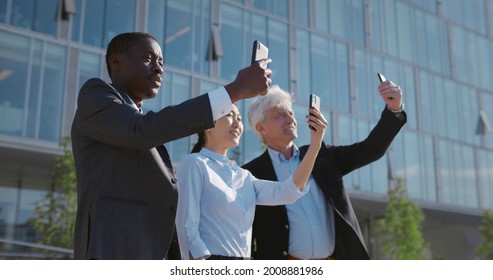 Medium Shot Of Diverse Business People Outside Taking Selfie On Smartphone. Multiethnic Colleagues Standing Outdoors Business Center Using Mobile Phone