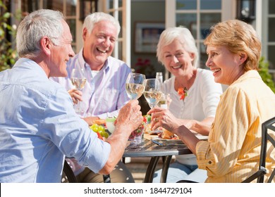 Medium Shot Of An Elderly Couple Having Lunch And Toasting Wine Glasses At The Patio Table With Friends.