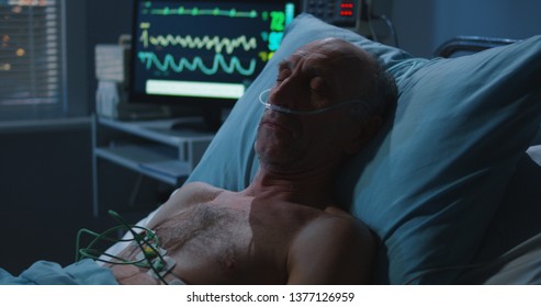 Medium shot of an elderly male patient sleeping and a heart monitor showing vital signs - Powered by Shutterstock