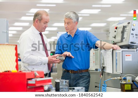 Medium shot of an engineer explaining the working of a machine part to a businessman in a manufacturing plant.