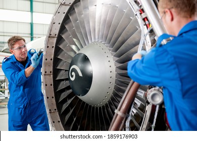 Medium shot of engineers repairing the turbine engine of a passenger jet at a hangar.