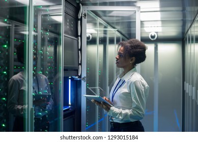 Medium shot of female technician working on a tablet in a data center full of rack servers running diagnostics and maintenance on the system
