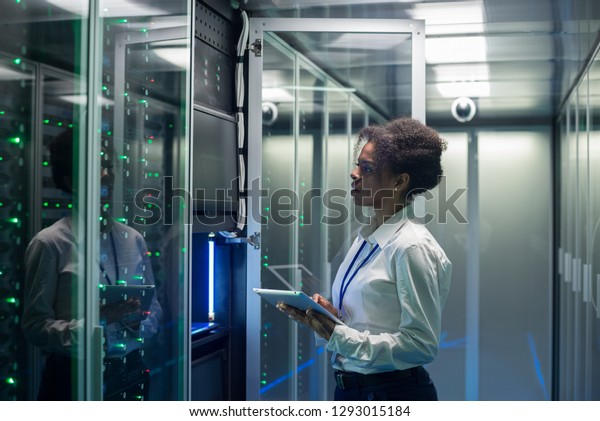 Medium shot of female technician working on a\
tablet in a data center full of rack servers running diagnostics\
and maintenance on the\
system