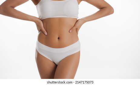 Medium shot of fit African American woman in white underwear puts her hands on her waistline on white background | Body care concept