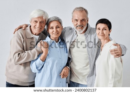 Medium shot of four smiling elderly friends with their arms around each other standing together at neutral background and looking at camera