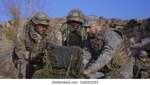 Medium Shot Of Fully Equipped And Armed African American Soldier Looking At A Computer And Another Talking On A Radio In The Field