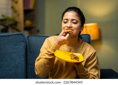 medium shot of girl enjoys eating tasty pizza by closing eyes at home on sofa - concept of yummy food, excitement and emotion or expression.