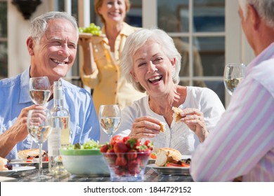 Medium shot of a happy elderly couple having lunch at a patio table with a woman carrying grapes in the background. - Powered by Shutterstock