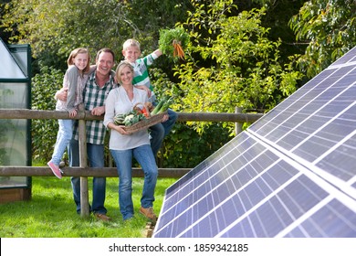 Eine mittelmäßige Aufnahme einer glücklichen Familie, die einen Korb Gemüse hält, während sie auf einer Garderobe in der Nähe eines großen Solarpaneels steht und sich anlehnt.