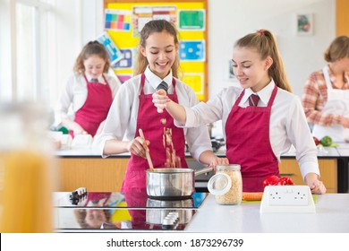 Medium shot of high school students in aprons cooking during a home economics class.