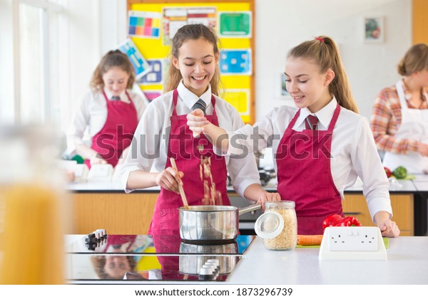 Medium shot of high school students in\
aprons cooking during a home economics\
class.
