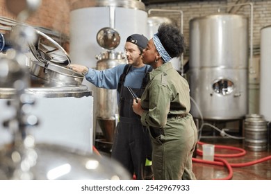 Medium shot of male factory worker opening lid of tank for female African American process technician to observe cider fermentation during quality inspection at plant, copy space - Powered by Shutterstock