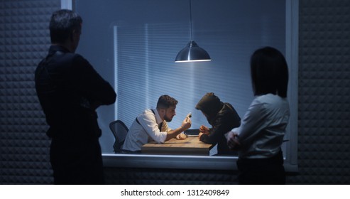 Medium shot of a male and a female investigator watching their colleague interrogating a drug dealer