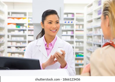 Medium Shot Of A Male Pharmacist With Medicine Standing At A Pharmacy Counter And Smiling At A Customer.