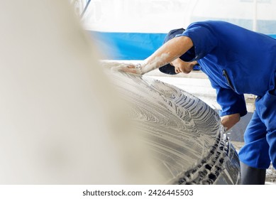 Medium shot of a man washing the front of a soapy car at a car wash, with copy space - Powered by Shutterstock