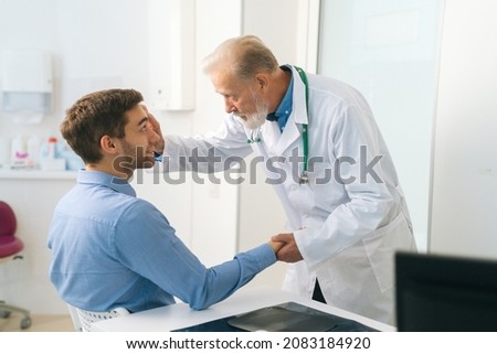 Medium shot of mature adult male ophthalmologist examining eyes of male patient during checkup visit in clinic office. Young man coming in for consultation before undergoing vision correction surgery.