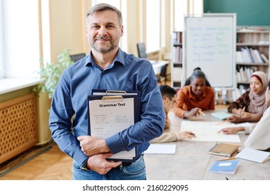 Medium shot of mature Caucasian man teaching English language holding clipboard with grammar tests looking at camera - Shutterstock ID 2160229095