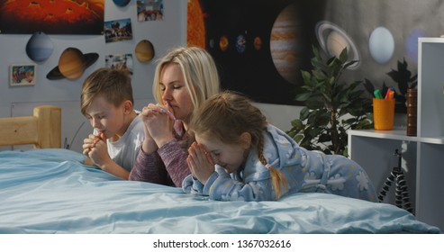 Medium Shot Of A Mother And Her Two Children Praying Together On A Bed