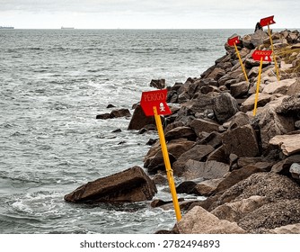 A medium shot at normal angle captures a rocky seaside slope, dotted with warning signs.