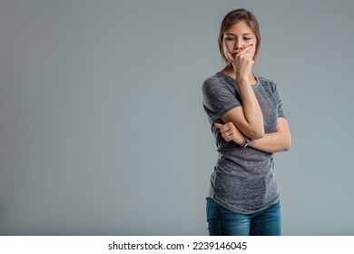 medium shot of a pretty young woman hides her mouth behind a gesture of someone reflecting intensely; she has either missed something or just had a disruptive idea that she does not intend to share be - Shutterstock ID 2239146045