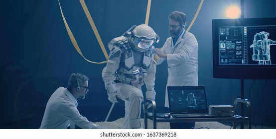 Medium shot of scientists adjusting anti-gravity bands on astronauts spacesuit for a low gravity test - Powered by Shutterstock