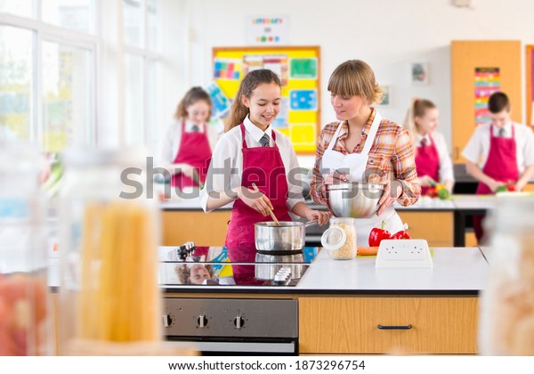 Medium shot of a teacher guiding her\
student while she cooks during a home economics\
class.