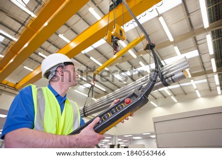 Medium shot of a technician wearing a helmet while operating hoist with raw aluminum in a hi-tech manufacturing plant.