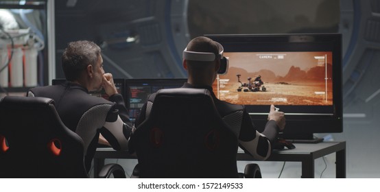 Medium shot of a VR headset wearing young man controlling Mars rover with remote controller in a base - Shutterstock ID 1572149533