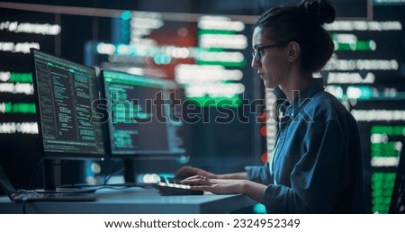 Medium Shot of Woman Working as a Developer, Surrounded by Big Screens Displaying Lines of Code in Dark Monitoring Room. Female Programmer Using Desktop Computer, Analysing Data, Creating AI Software