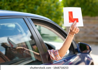 A Medium Shot Of A Woman's Hand Holding A Learner's Permit Sticker Out Of A Car Window.