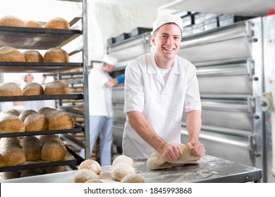 A medium shot of a young baker smiling and looking the camera while kneading bread dough in a bakery.