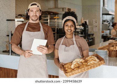 Medium shot of young biracial bakery workers standing against counter smiling at camera - Powered by Shutterstock