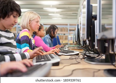 A Medium Shot Of A Young Blonde Girl Using Computer In A School Computer Lab With Other Students.