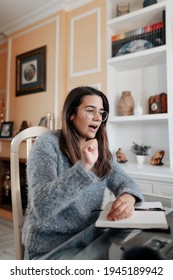 Medium shot young deaf woman wearing glasses and a sweater is using sign language to spell name while in an online video call in her living room. - Shutterstock ID 1945189942