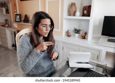 Medium shot young deaf woman wearing glasses and a sweater is using sign language to spell name while in an online video call in her living room. - Shutterstock ID 1945189945