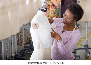 Medium shot of a young design student of African ethnicity measuring a garment worn by a mannequin. - Powered by Shutterstock