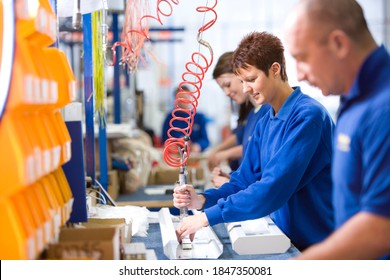 A medium shot of a young female worker working on an aluminum light fittings on the production line with other workers. - Shutterstock ID 1847350081