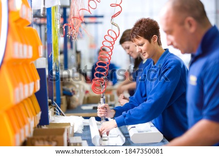 A medium shot of a young female worker working on an aluminum light fittings on the production line with other workers.