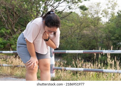 Medium shot, young obese Asian woman standing at outdoor park, resting after running, unable to breathe, suffering from respiratory problem. Health issues, heart attack, heat stroke, obesity concept.