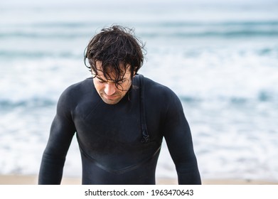 Medium shot young wet man with diving suit getting out of the sea looking down. - Powered by Shutterstock