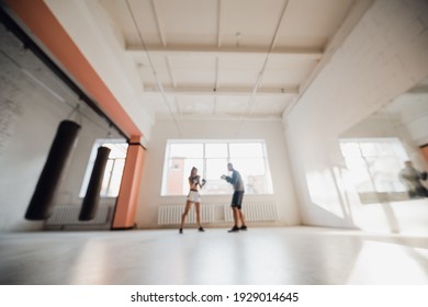 Medium shot of young woman doing boxing workout at the gym and punching her instructor, who is dodging her blows and controlling training process.