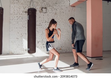 Medium shot of young woman doing boxing workout at the gym and punching her instructor, who is dodging her blows and controlling training process. - Shutterstock ID 2093814073