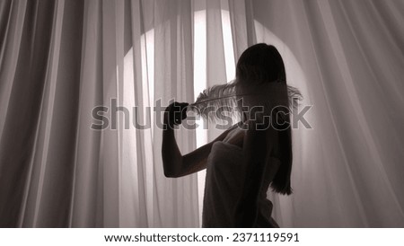 Medium side view shot of a young woman's silhouette wrapped in a towel touching and stroking her neck and body with a white feather.