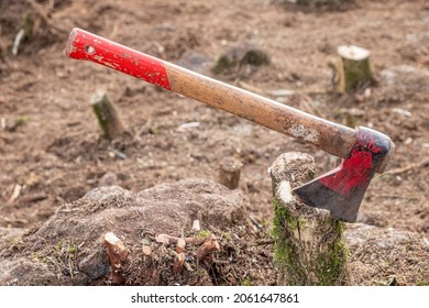 Medium sized axe with red painted parts and wooden handle nailed to a stump.