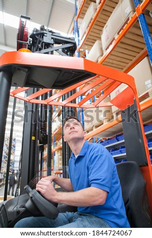 Medium vertical shot of a worker operating a forklift at the production line of a distribution warehouse.