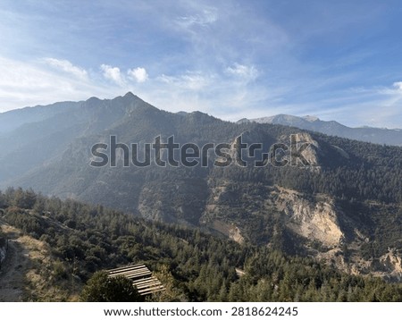 Medium view of rugged mountain peaks above forested slopes with a tiny cabin in valley.