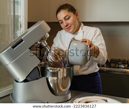 medium-adult woman pastry chef adding flour in planetary mixer, owner of her own business