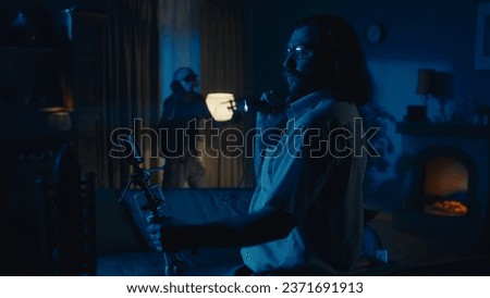Medium-full photo capturing two ghost hunters entering a dark room in search for an entity that's making the lights flash, filming the surroundings on camera.