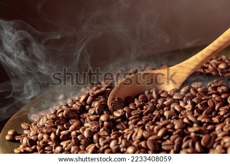 Medium-roasted coffee beans are smoky in a roasting pan. Copy space.
