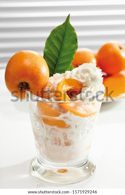 Medlar,\
whole and halved in a glass with whipped\
cream